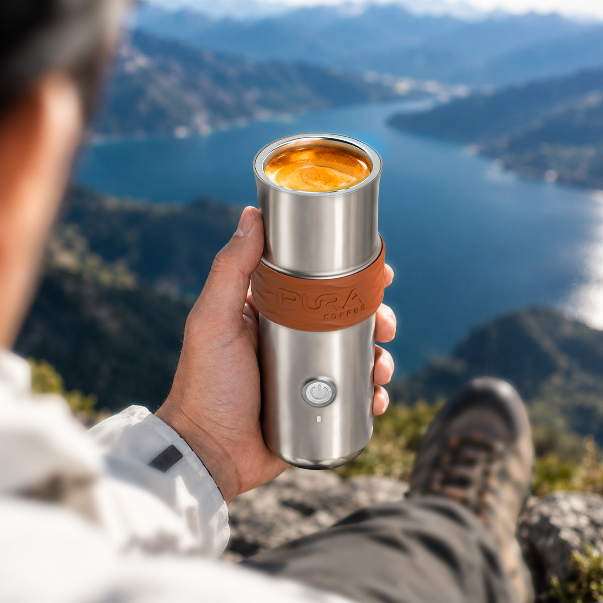 Hand holding the PURA NEO Pro with fresh espresso on a mountaintop overlooking a lake